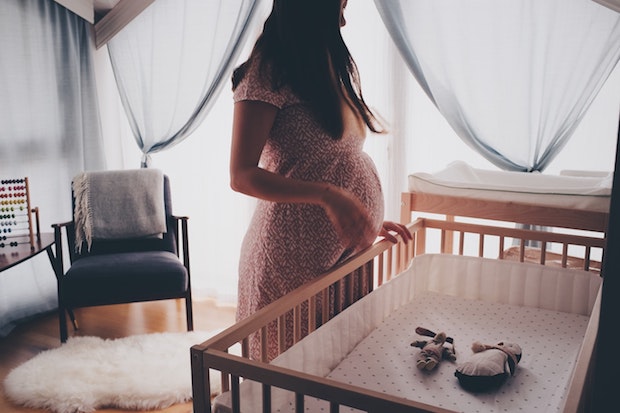 A pregnant lady overlooks a child’s cot