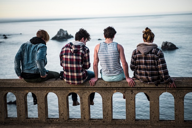 A group of teenagers sitting on a wall with their backs to the camer
